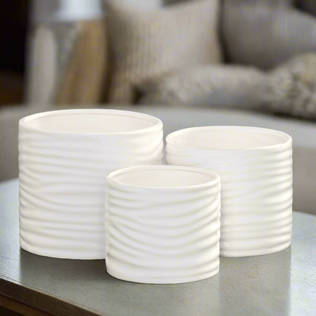 Three white ceramic pots with textured design on a reflective surface.