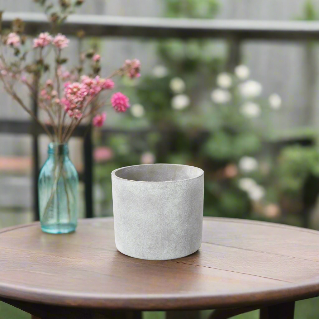 Concrete planter on a wooden table with pink flowers and a blurred garden background