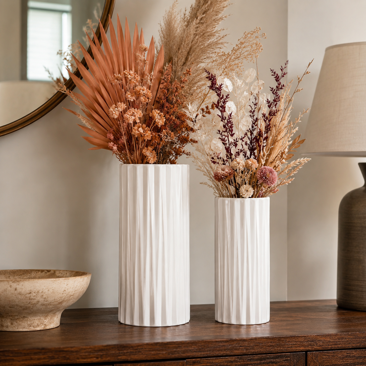 Two white ribbed ceramic vases filled with dried botanicals, displayed on a dark wood console table in a styled interior setting.