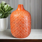 Orange textured vase on a surface with a blurred plant in the background