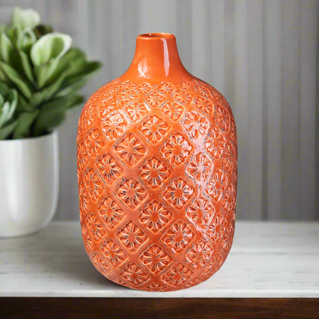 Orange textured vase on a surface with a blurred plant in the background