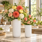 Two white textured ceramic vases filled with a colorful floral arrangement on a marble countertop in a bright, modern kitchen setting.