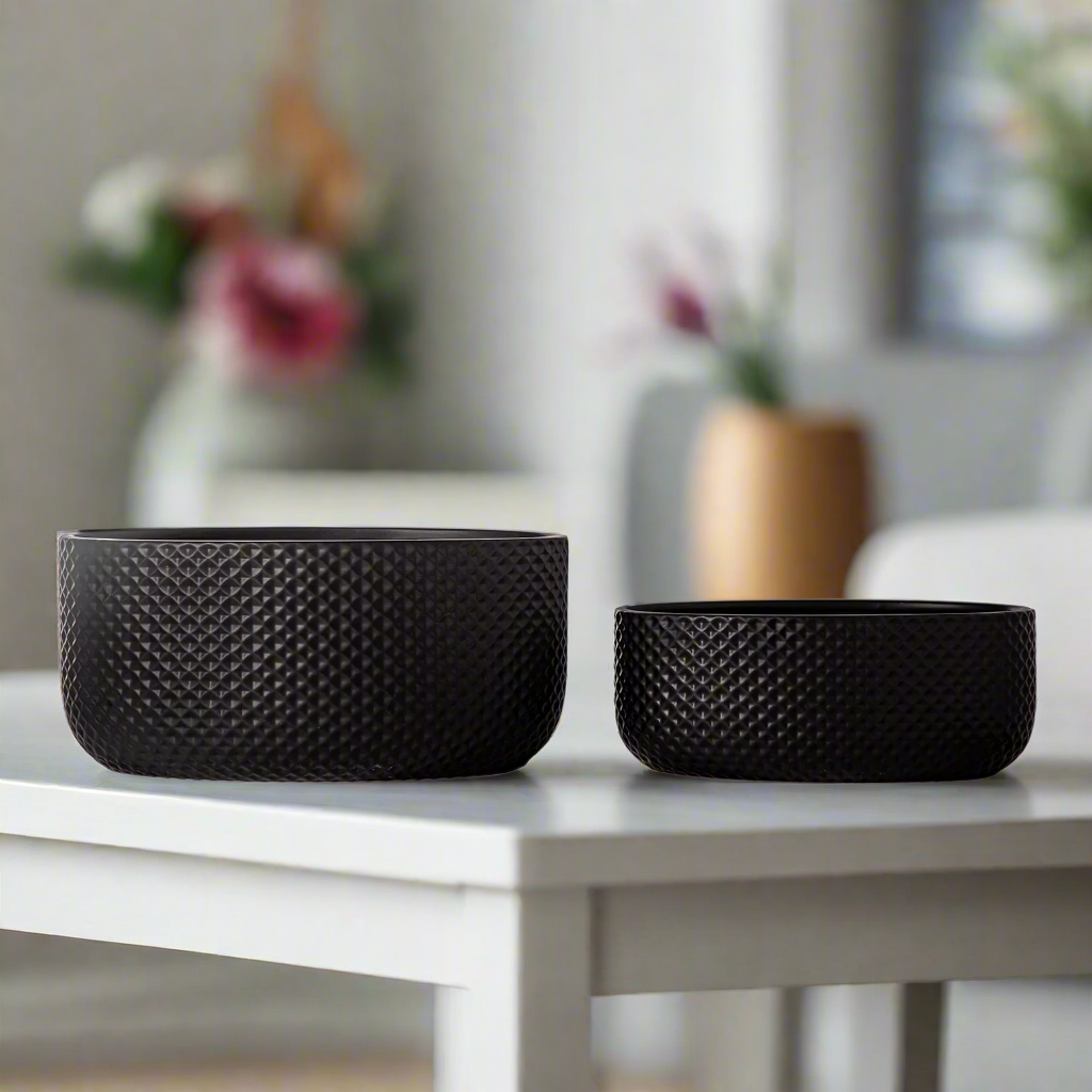 Two black textured bowls on a white table with a blurred background