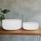 Two white woven bowls on a wooden surface with a blurred background