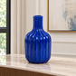 A glossy cobalt blue ribbed vase with a narrow neck, displayed on a light marble console table in a modern room setting.