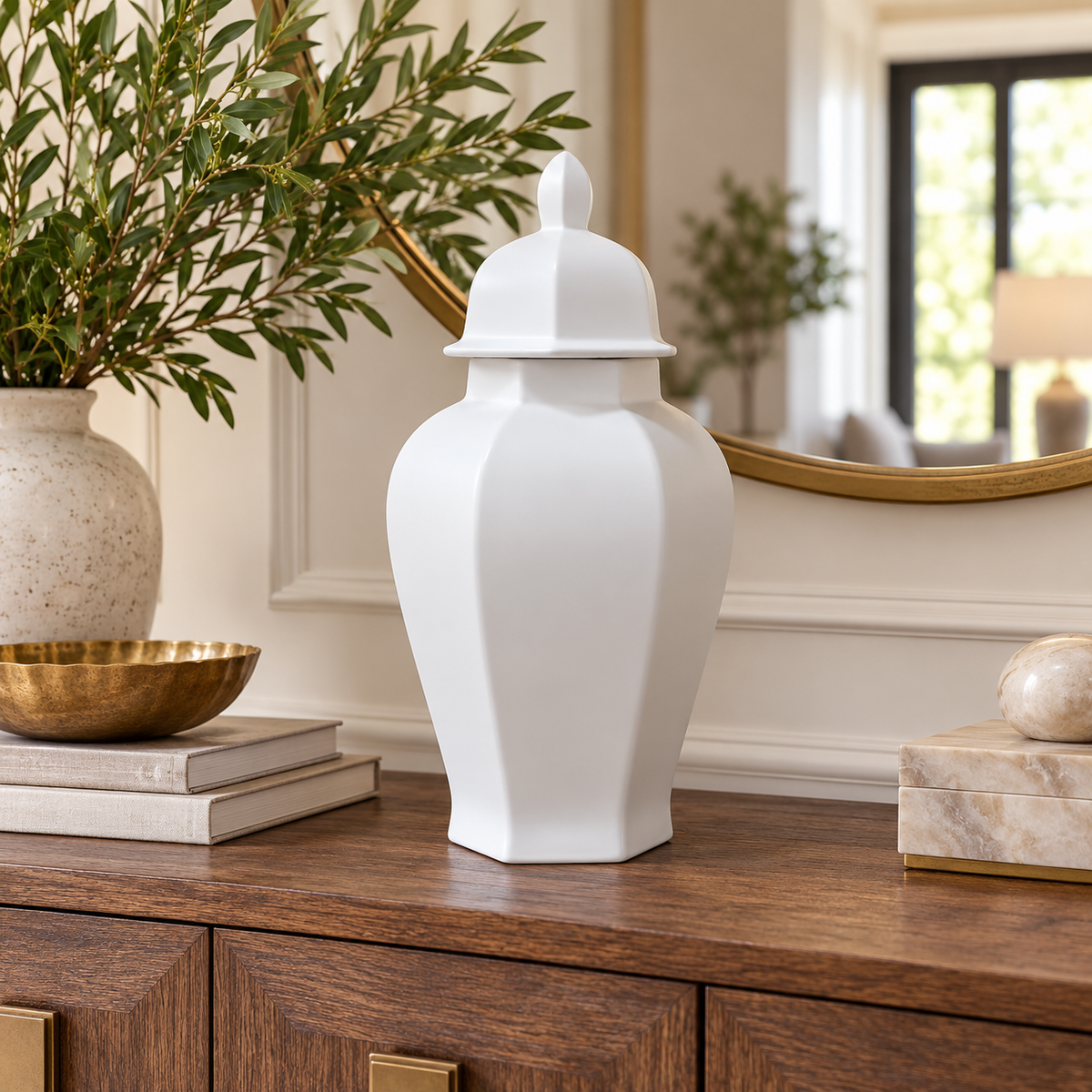 A white ceramic lidded storage jar with a geometric faceted design, displayed on a dark wood console table in a styled home interior.