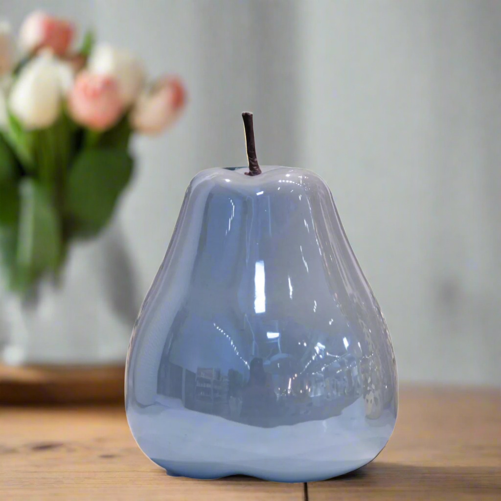 Blue ceramic pear-shaped object on a wooden surface with a blurred floral arrangement in the background.