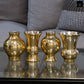 Four gold metallic vases on a reflective surface with a blurred background