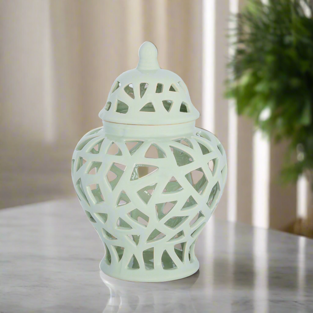 Decorative light green vase with intricate lattice design on a reflective surface.
