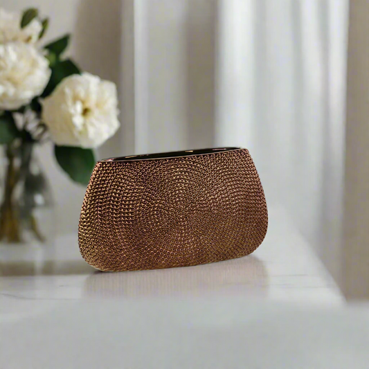 Bronze clutch bag on a light surface with white flowers in the background
