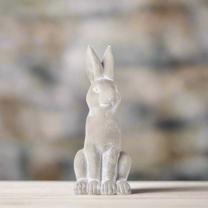 Gray rabbit figurine on a wooden surface with a blurred natural background