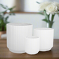 Set of three white ribbed planters on a wooden surface with a blurred background
