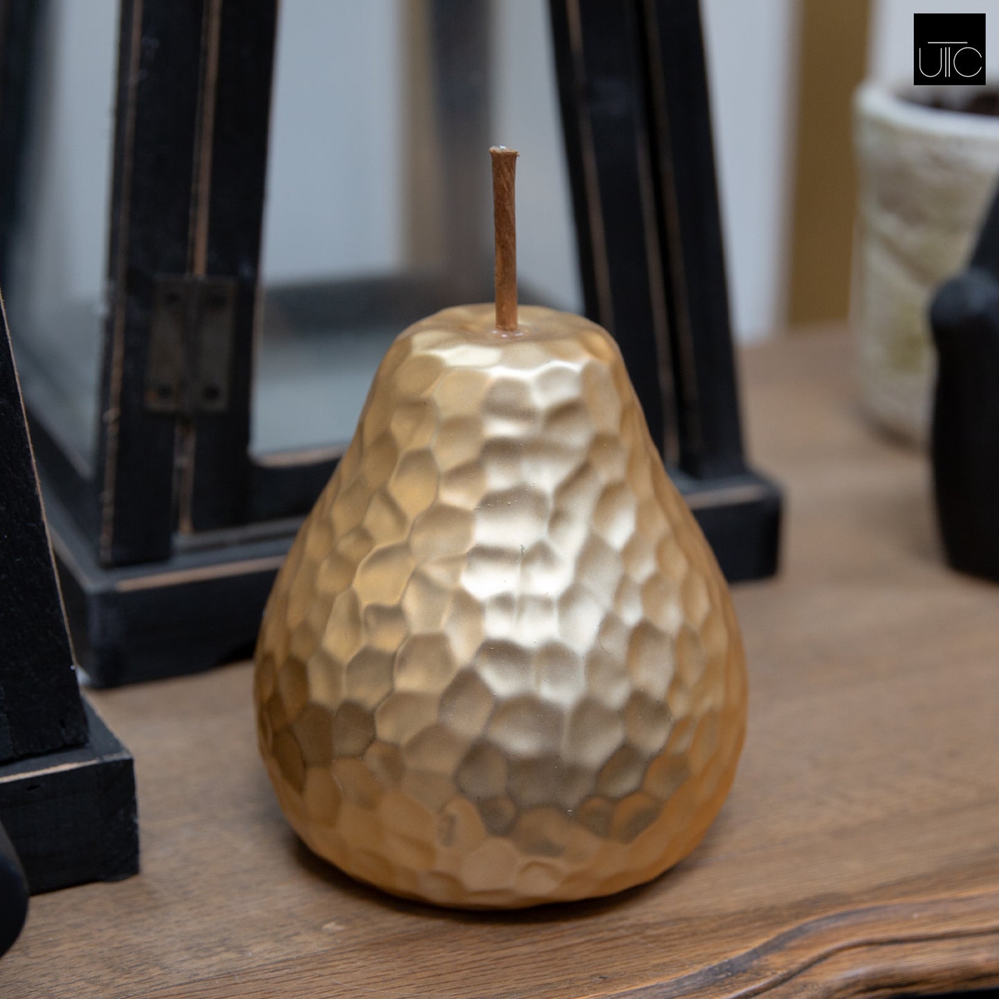 A gold-colored ceramic pear figurine with a hammered design and stem, placed on a wooden surface.