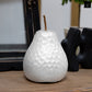 A gold-colored ceramic pear figurine with a hammered design and stem, placed on a wooden surface.