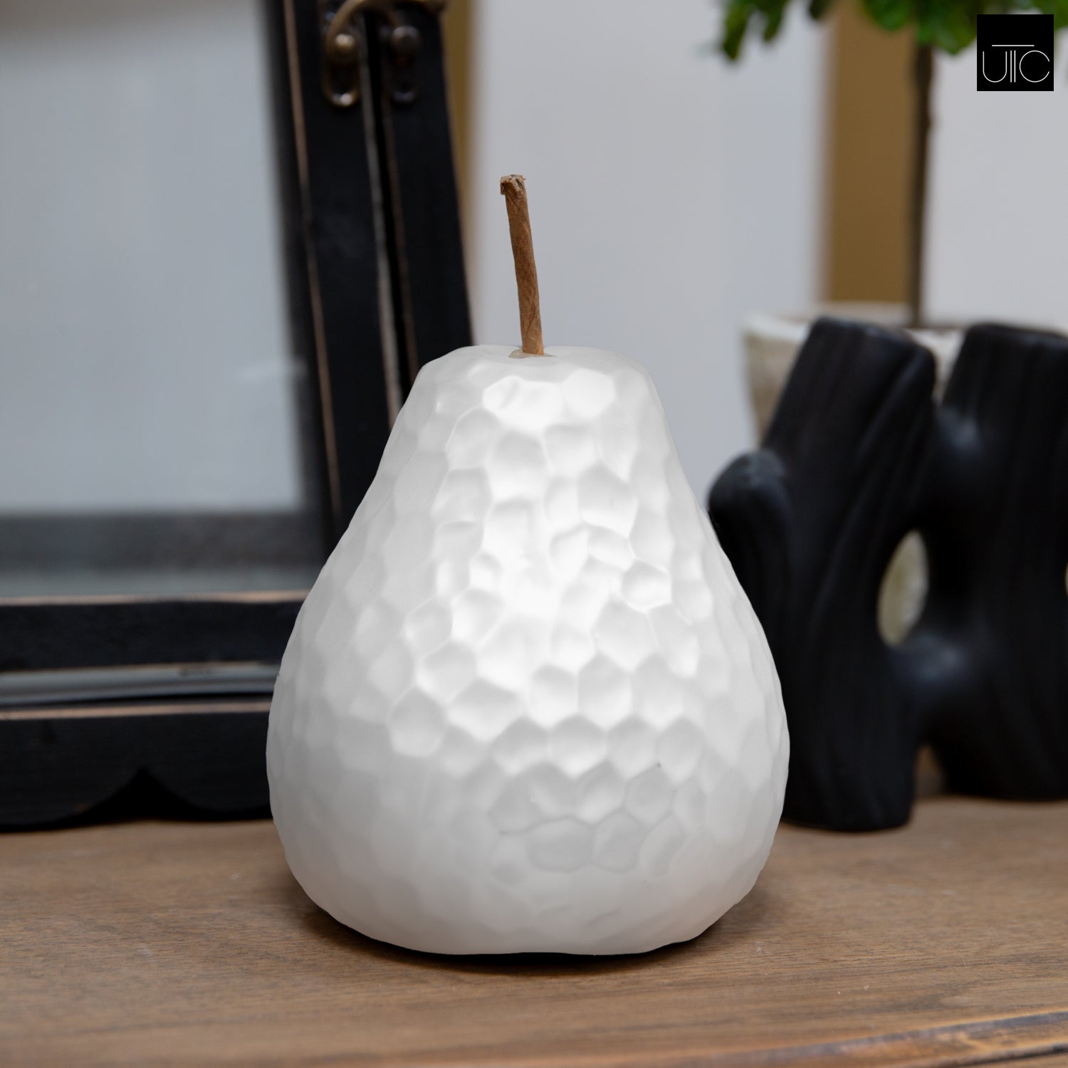 A gold-colored ceramic pear figurine with a hammered design and stem, placed on a wooden surface.