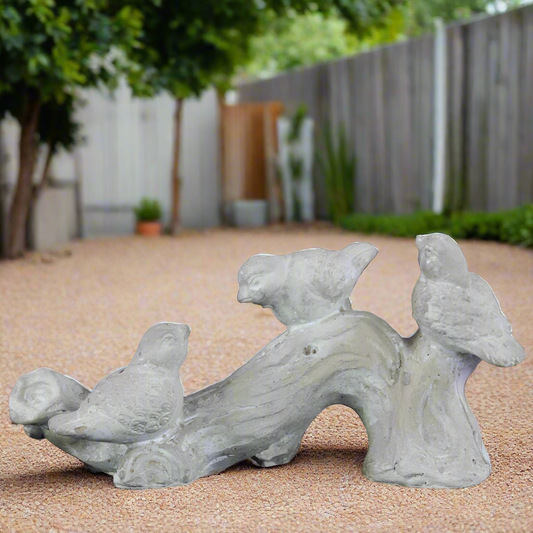 A white terracotta sculpture of tree branches with three bird figurines, set against an outdoor background.