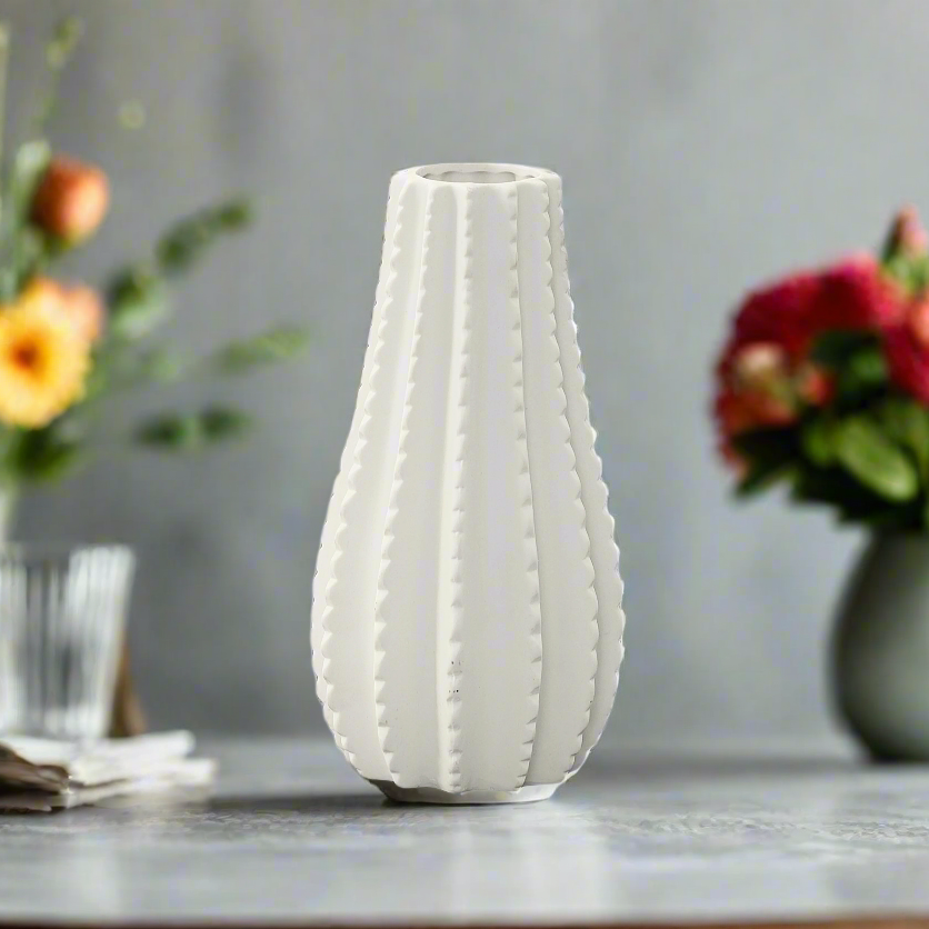 White textured vase on a table with floral arrangements in the background