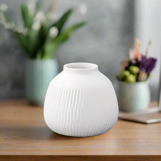 White textured vase on a wooden surface with blurred plants in the background