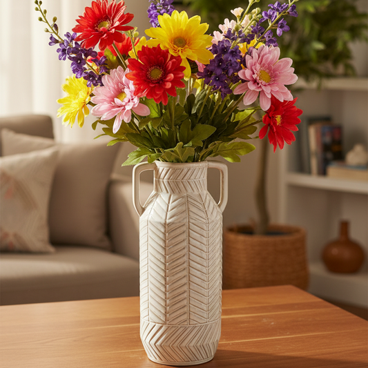 A colorful artificial flower bouquet in a textured white ceramic vase, placed on a wooden table in a cozy living room setting.