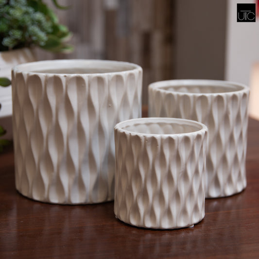 A set of three white ceramic cylindrical pots with embossed wave designs, displayed on a wooden surface.