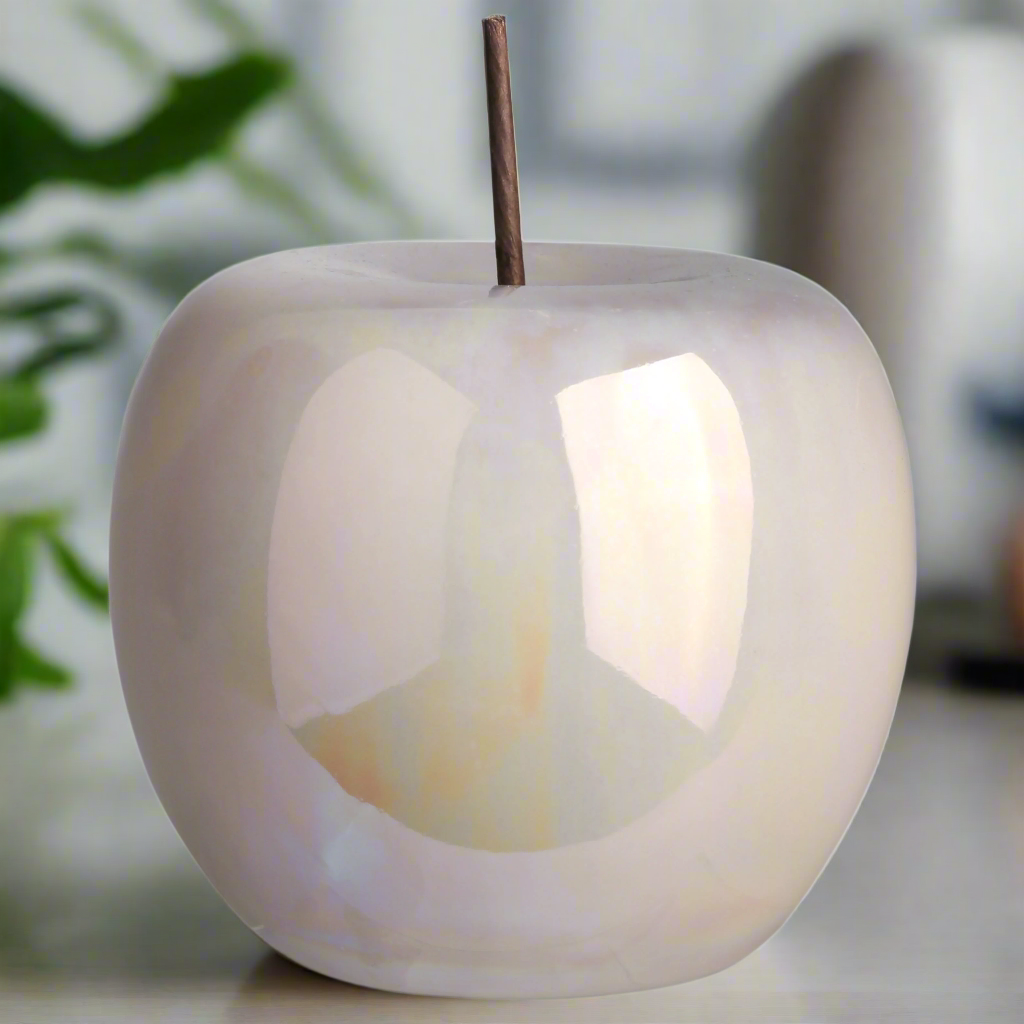 White ceramic apple-shaped candle holder with a lit candle inside, blurred background