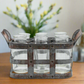 Metallic holder with six clear glass jars on a wooden surface with a blurred floral background