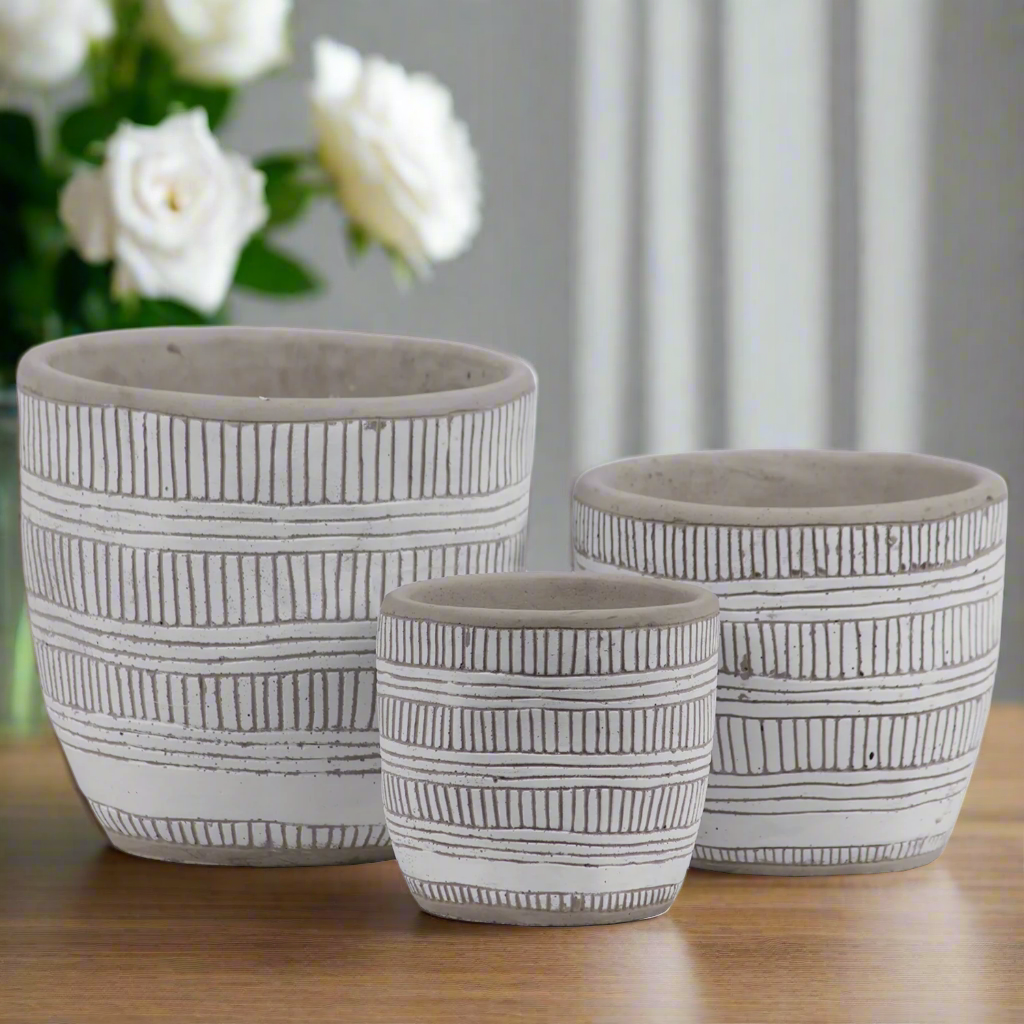Three ceramic pots with black line patterns on a wooden surface, with white flowers in the background.