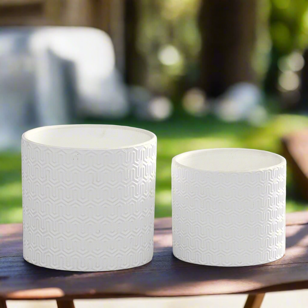 Two white textured planters on a wooden surface with a blurred outdoor background