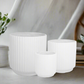 Three white textured planters on a light surface with a blurred background