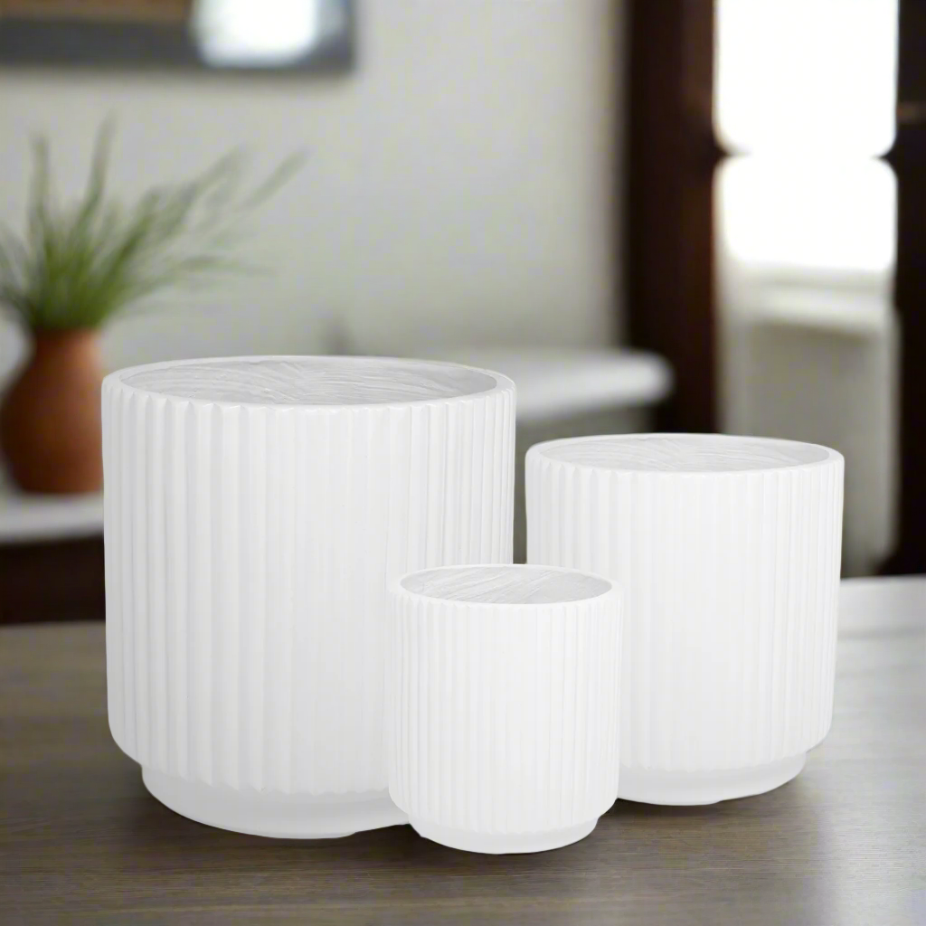 Three white ribbed planters on a surface with a blurred indoor background