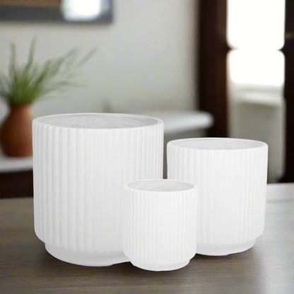 Three white ribbed planters on a surface with a blurred indoor background