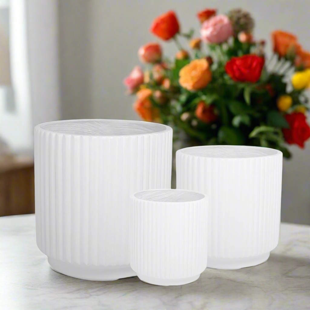 Three white ribbed planters on a marble surface with a bouquet of flowers in the background.