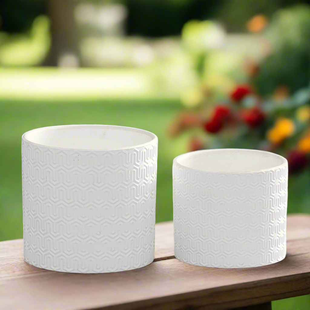 Two white textured planters on a wooden surface with a garden background