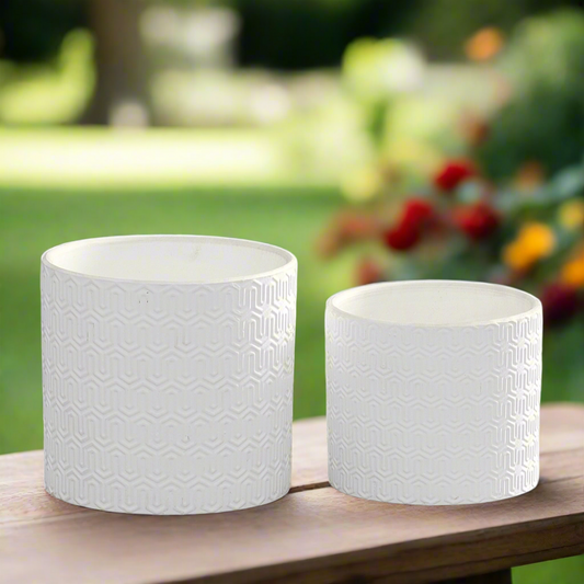 Two white textured planters on a wooden surface with a garden background