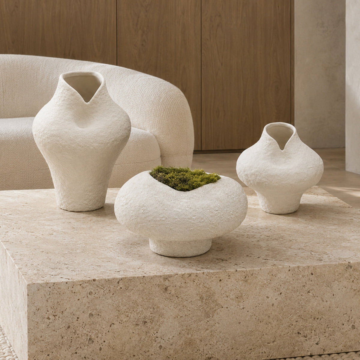 Three textured off-white ceramic vases in different shapes displayed on a stone coffee table in a modern, minimalist living room.