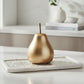 Gold pear-shaped object on a white marble tray with a neutral background