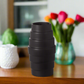 Black textured vase on a wooden surface with colorful tulips in the background