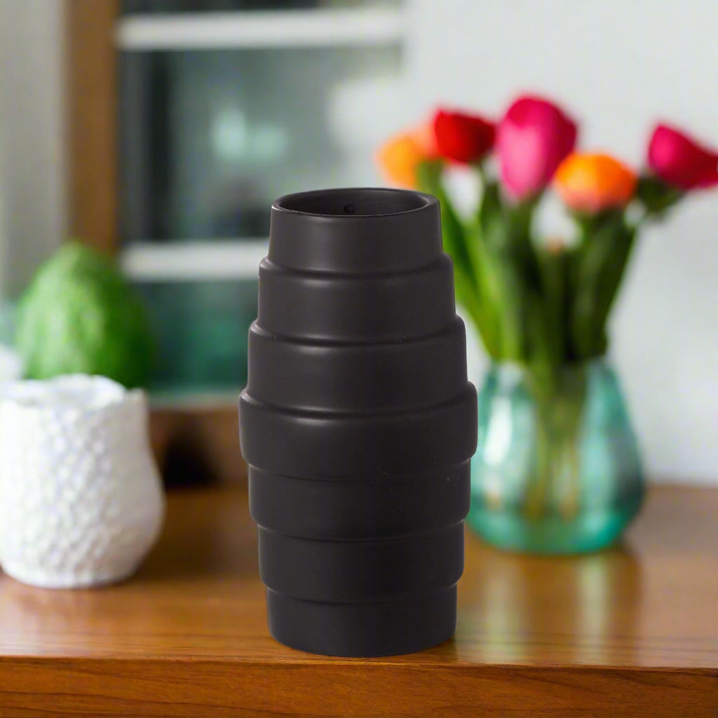 Black textured vase on a wooden surface with colorful tulips in the background