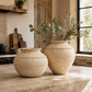 Two round beige ceramic vases with rope-like decorative bands, one filled with eucalyptus branches, displayed on a stone kitchen counter.